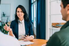 une femme devant un bureau fait face à deux hommes pour signer un docuement