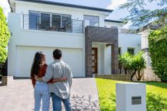 Un jeune couple enlacé admire la maison neuve qu'il vient d'acquérir